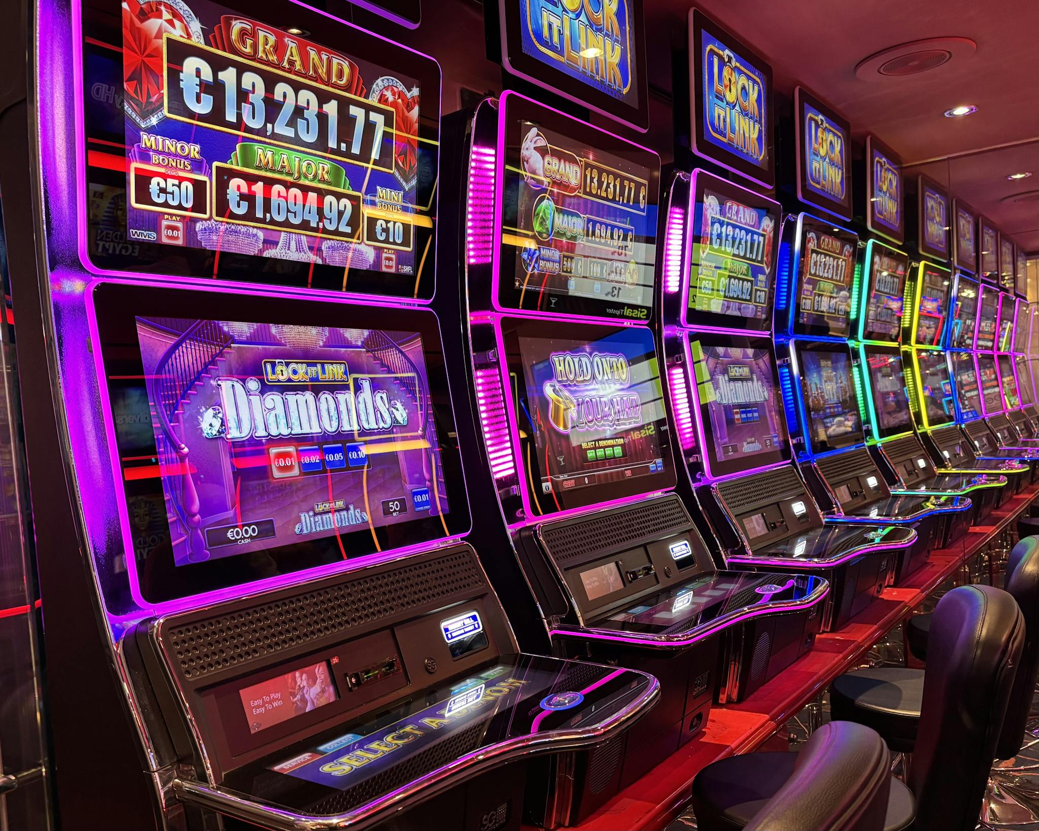 Colorful slot machines lined up in a casino with neon lights and jackpot displays.